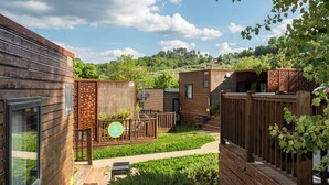 Una cabaña moderna de madera con terraza, rodeada de vegetación exuberante y cielo despejado.