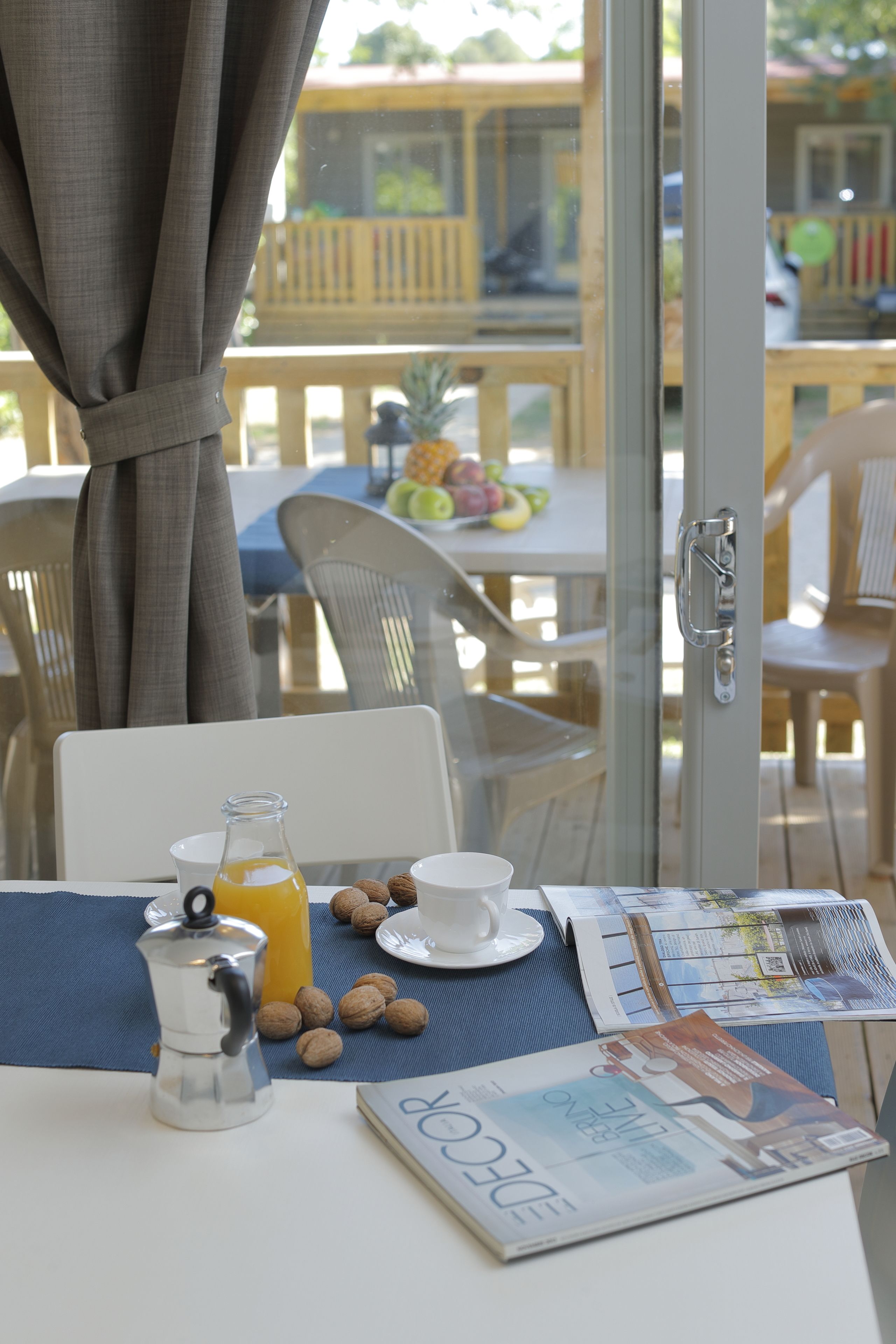 A breakfast table with a coffee pot, a glass of orange juice, a cup, a plate with walnuts, and a magazine.