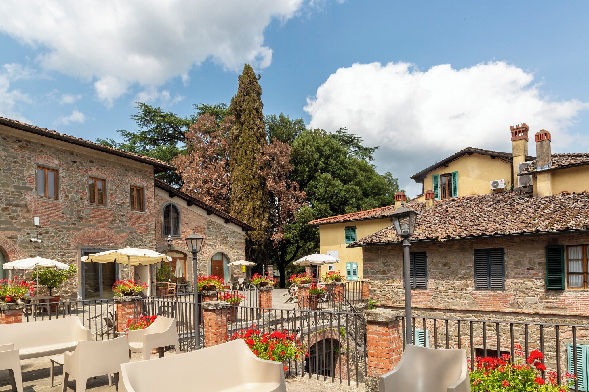 Un patio con edificios de piedra, mobiliario exterior y arreglos florales.