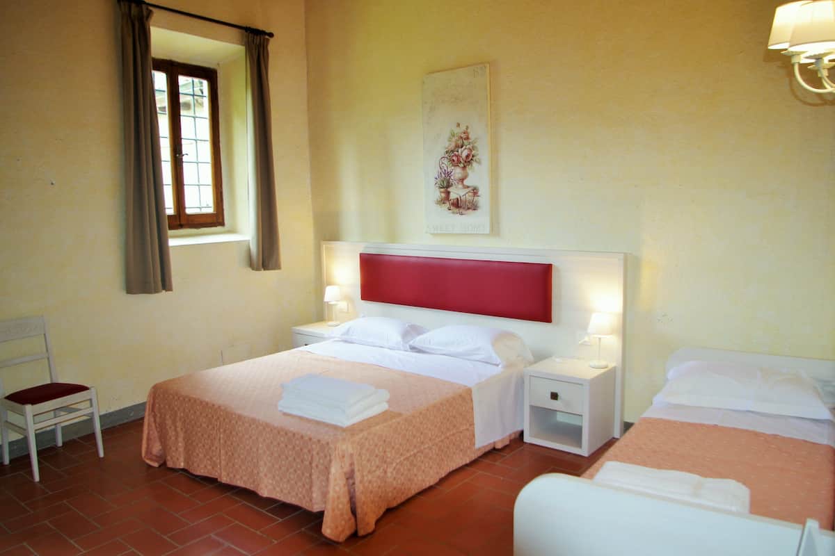 Una habitación de hotel con dos camas, una ventana con cortinas, una mesita de noche con lámpara y una silla.