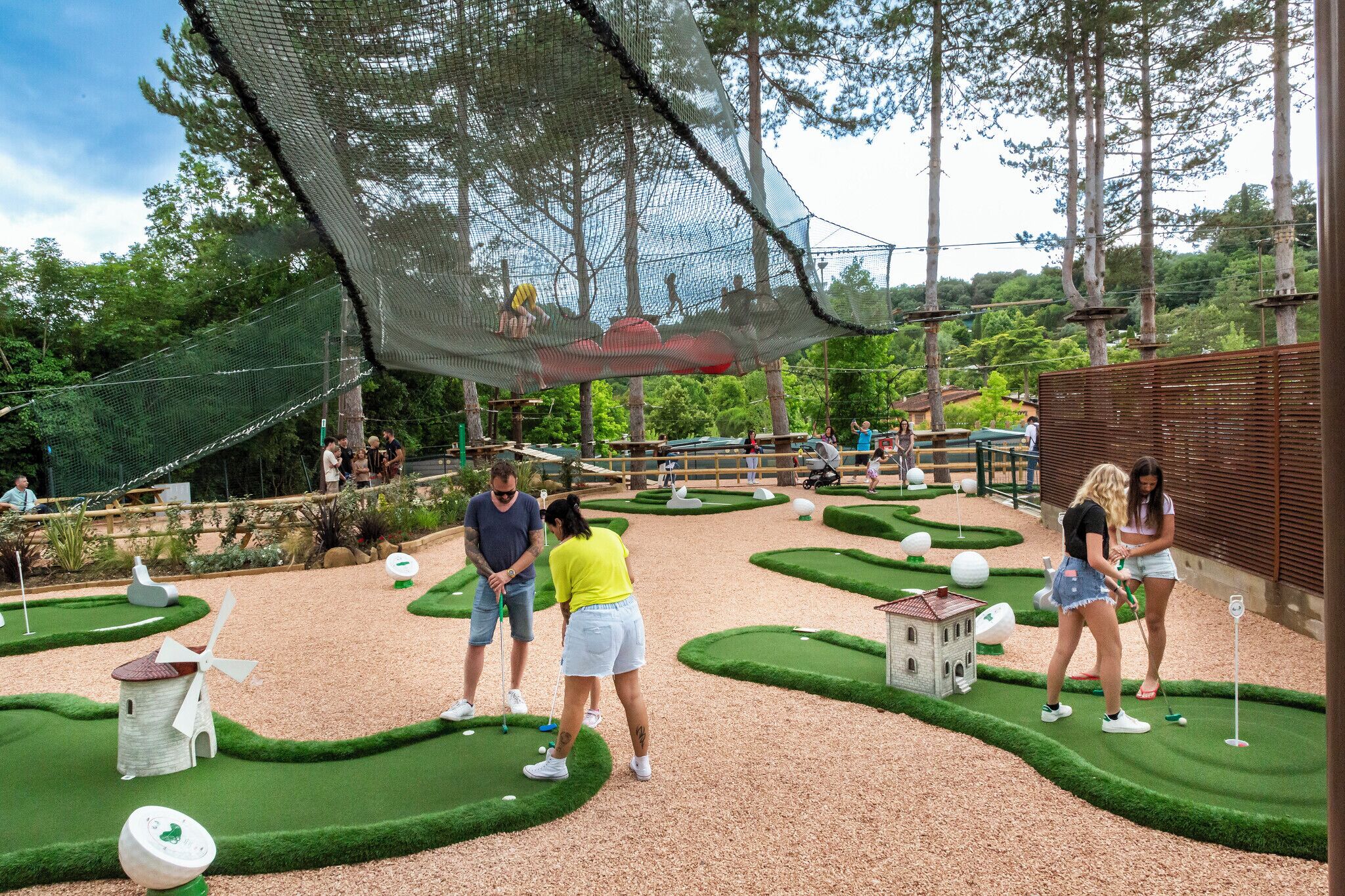 A miniature golf course with green fairways, a windmill, and a small building.