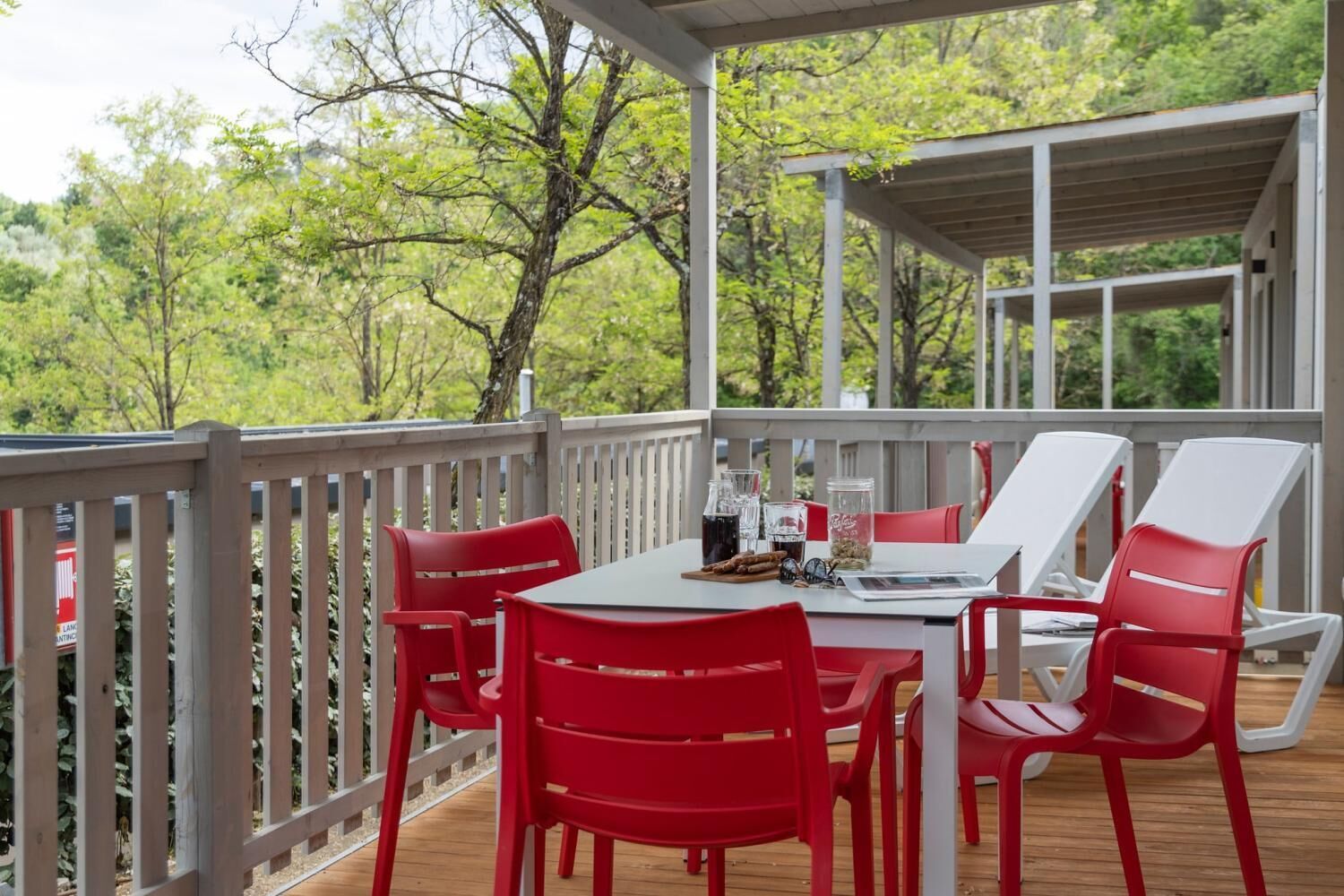 A covered outdoor deck with a table and red chairs, surrounded by a wooden deck and a white railing.