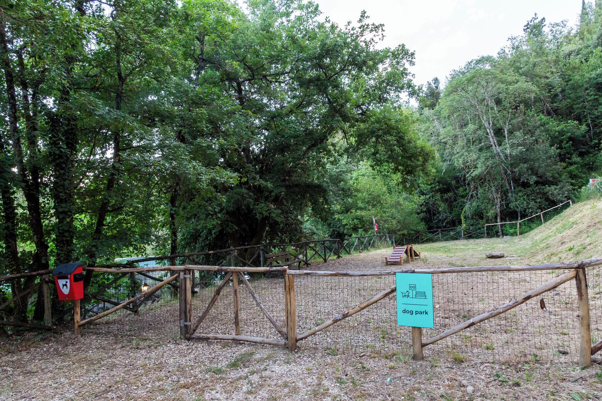 Un parc canin clôturé, doté d’une porte en bois, d’une boîte aux lettres rouge et d’un panneau indiquant la fonction du parc.