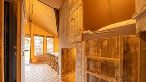 Interior de madera con techo alto, una puerta de madera y vista a una terraza exterior con sillas.