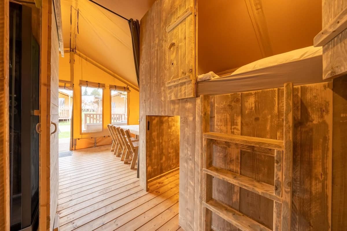 Interior de madera con techo alto, una puerta de madera y vista a una terraza exterior con sillas.