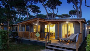 Una cabaña de madera con terraza, zona de comedor y sala de estar con mesa y sillones.