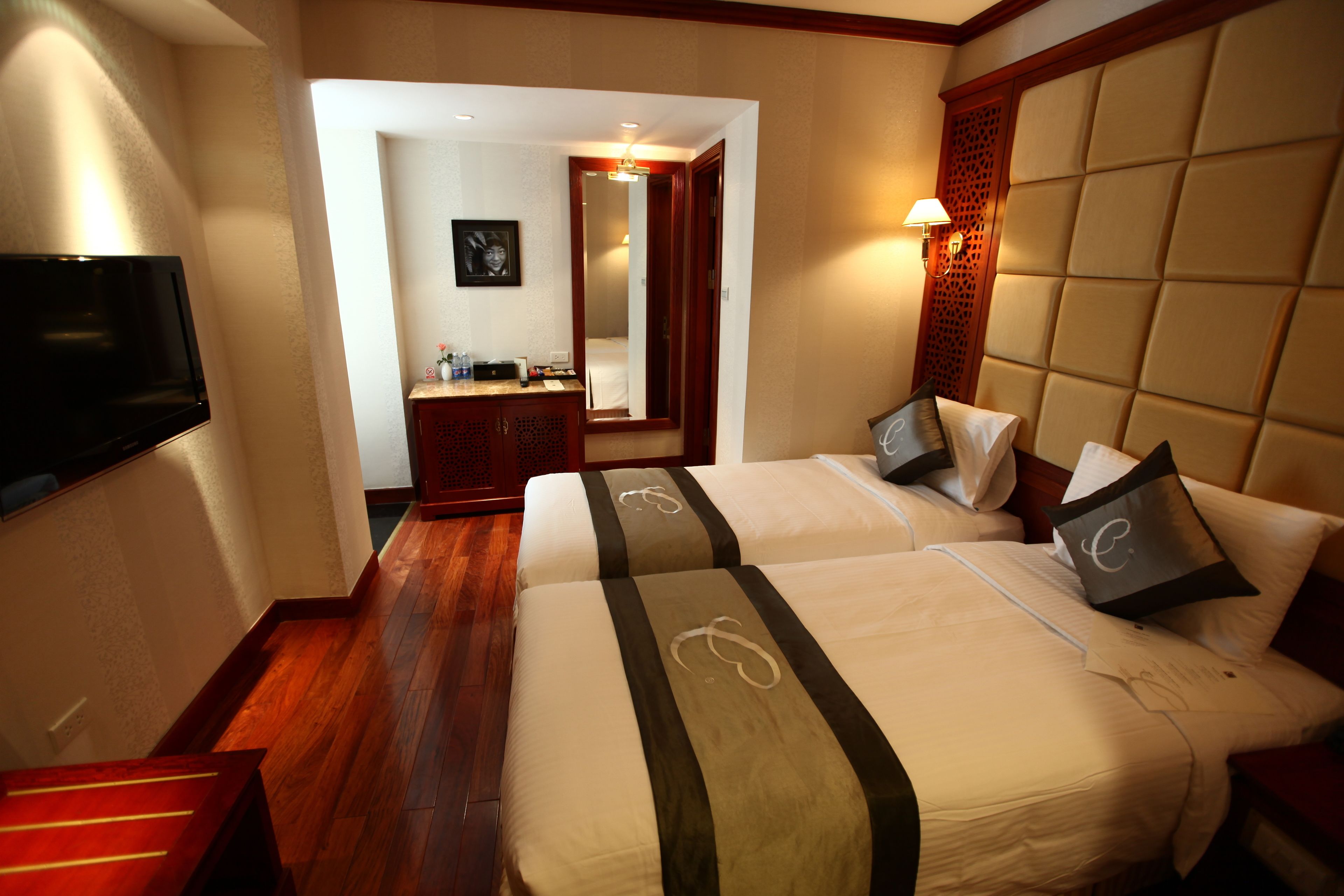 A hotel room with two beds, a TV, a mirror, and a wooden floor.
