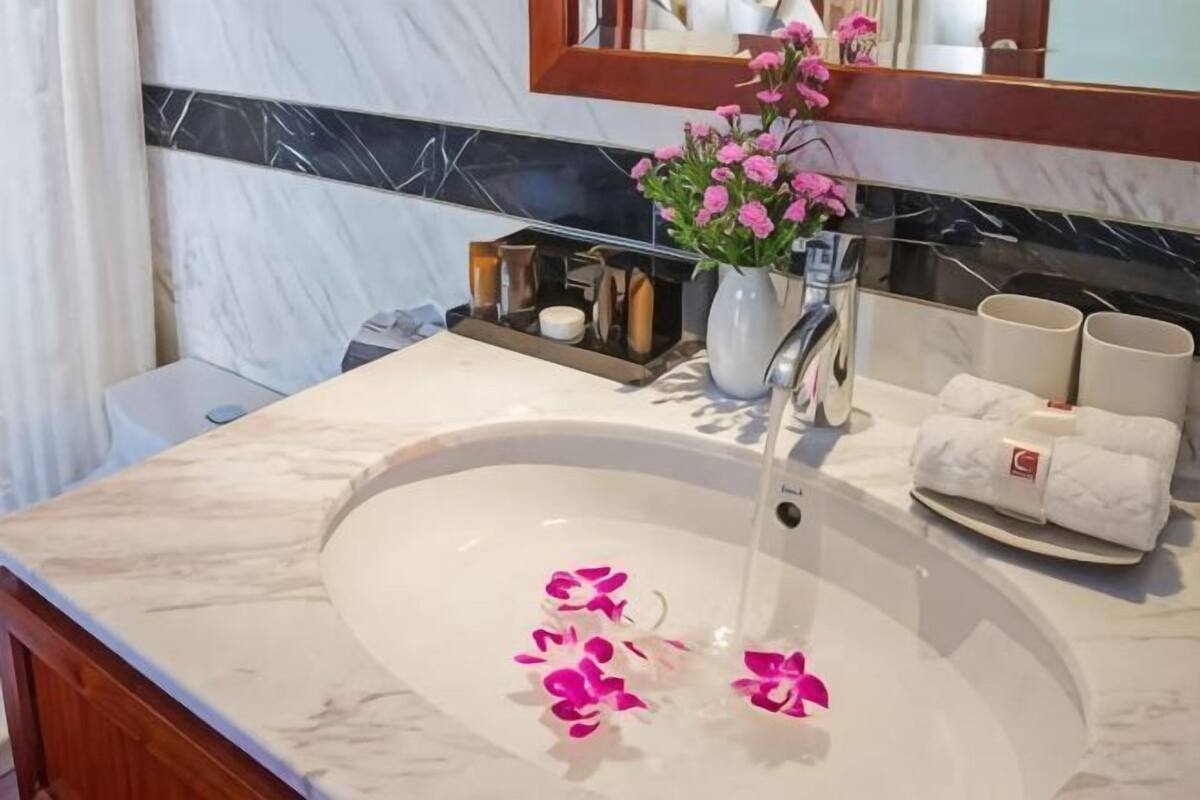 Un baño con lavamanos de mármol, un jarrón de flores rosas y un toallero con toallas dobladas.