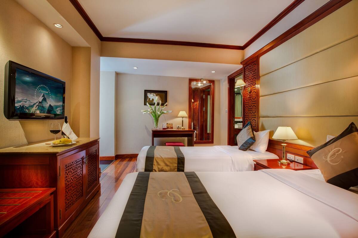 Habitación de hotel con dos camas, un televisor, un escritorio y un espejo decorativo.