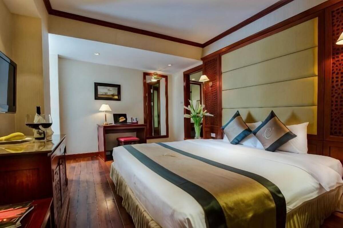 Una habitación de hotel con una cama grande, un escritorio con lámpara, una silla y un espejo.