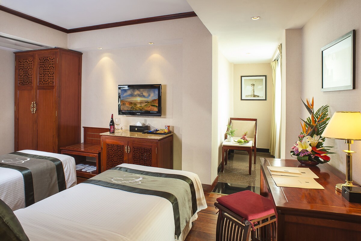 A hotel room with two beds, a desk with a lamp, a television, and a cabinet.