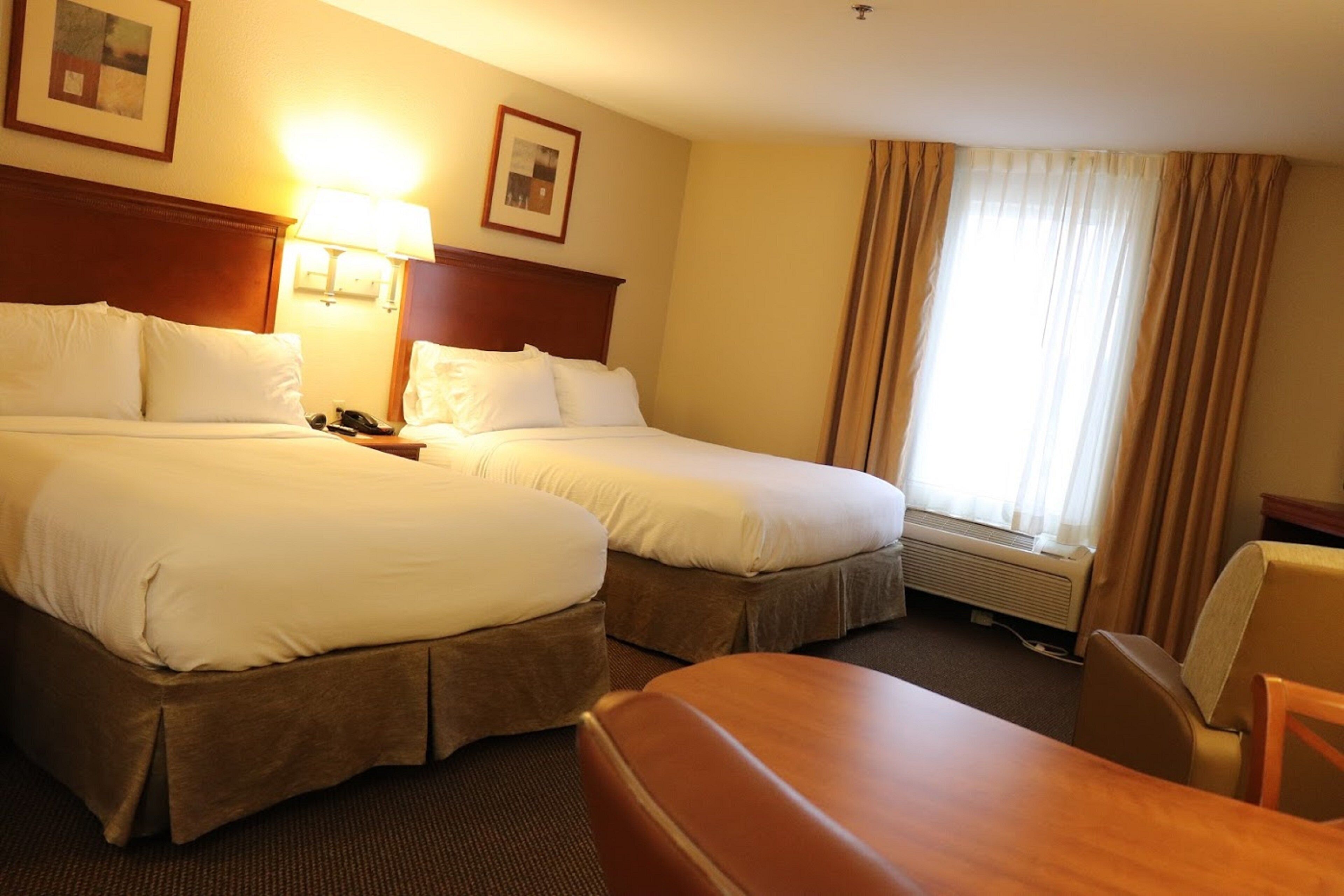 Ein Hotelzimmer mit zwei Betten, einem Schreibtisch, einem Stuhl, einer Lampe und einem Fenster mit Vorhängen.