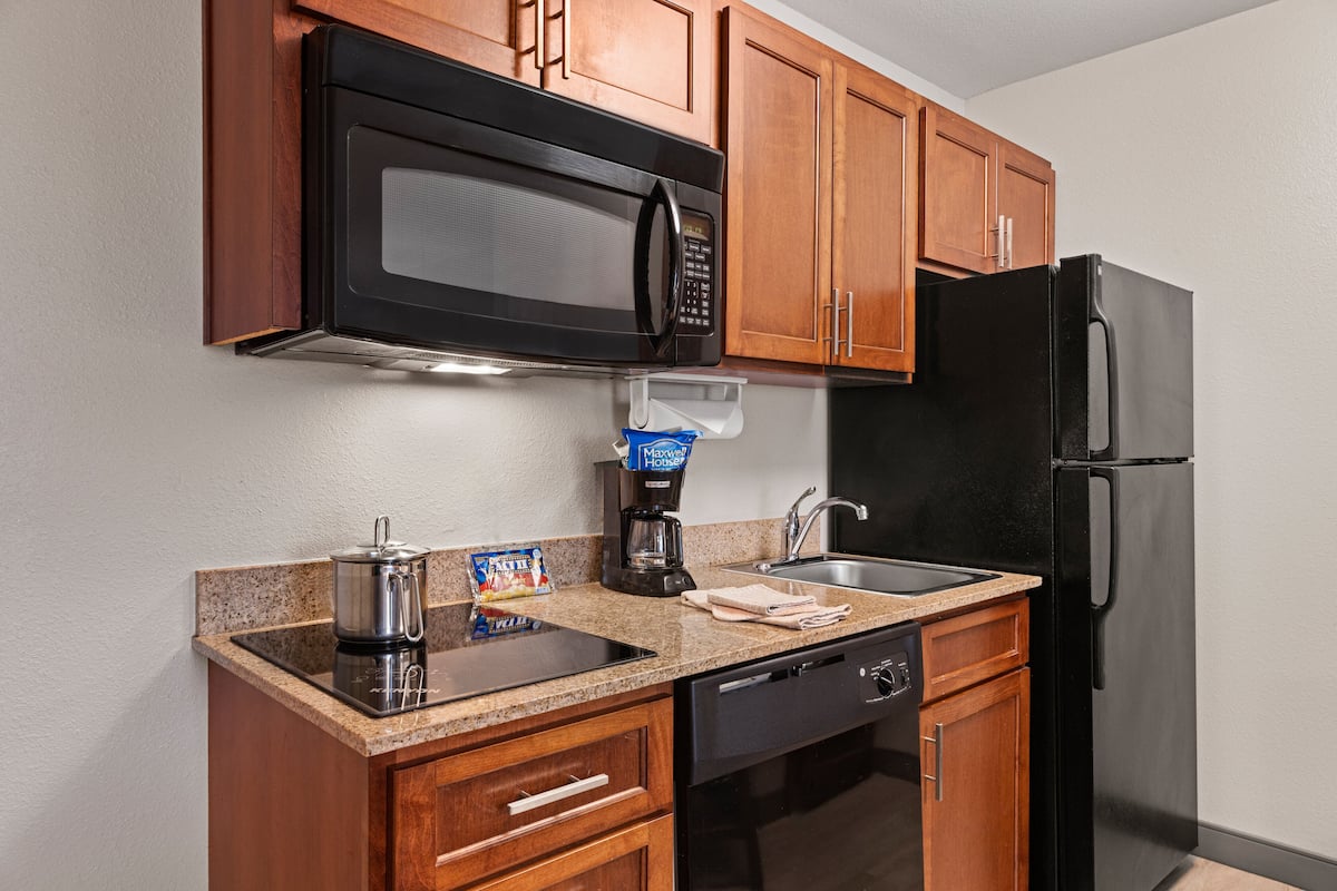 A compact kitchen with wooden cabinets, a black microwave, a coffee maker, a refrigerator, and a dishwasher.