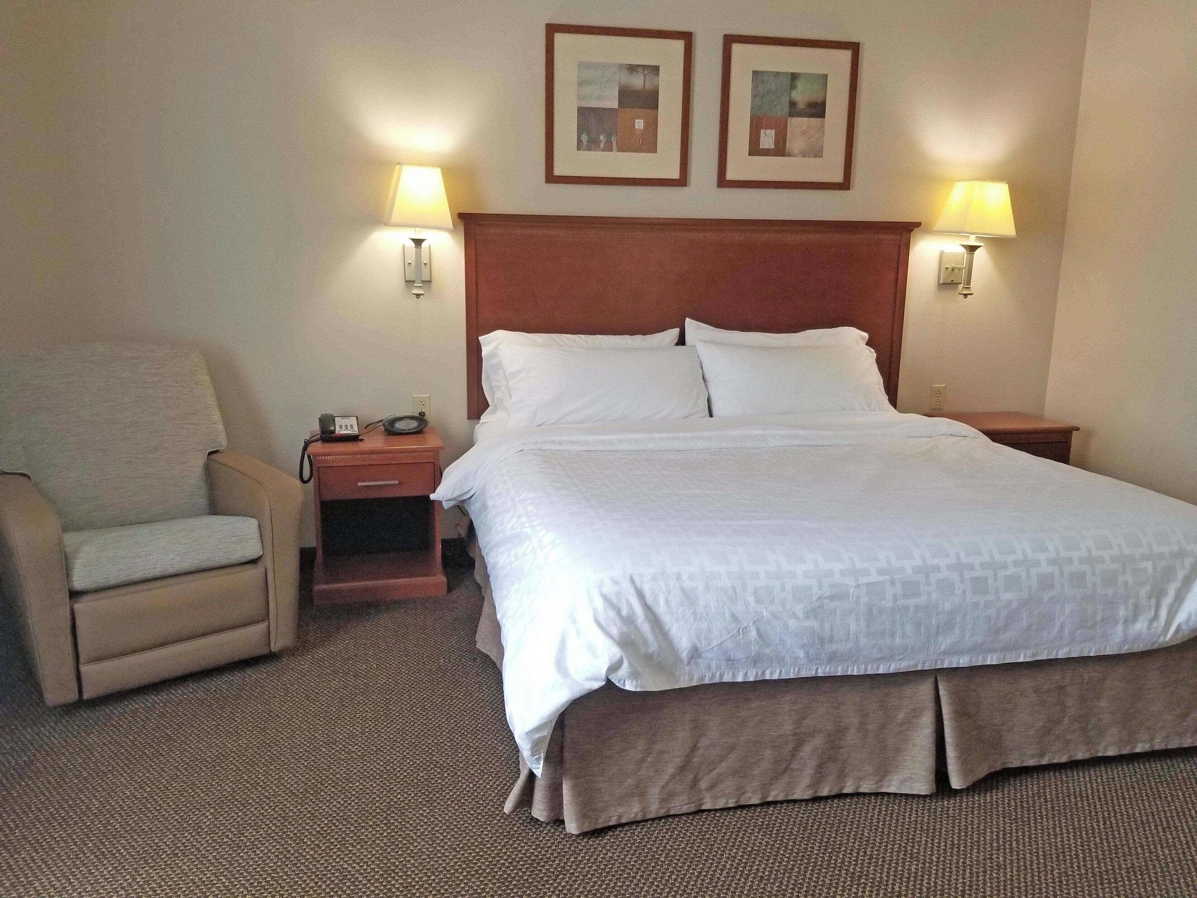 A hotel room with a bed, a chair, two bedside lamps, and a nightstand with a telephone.