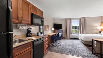 A hotel room with a kitchenette, a bed, a desk, and a TV.