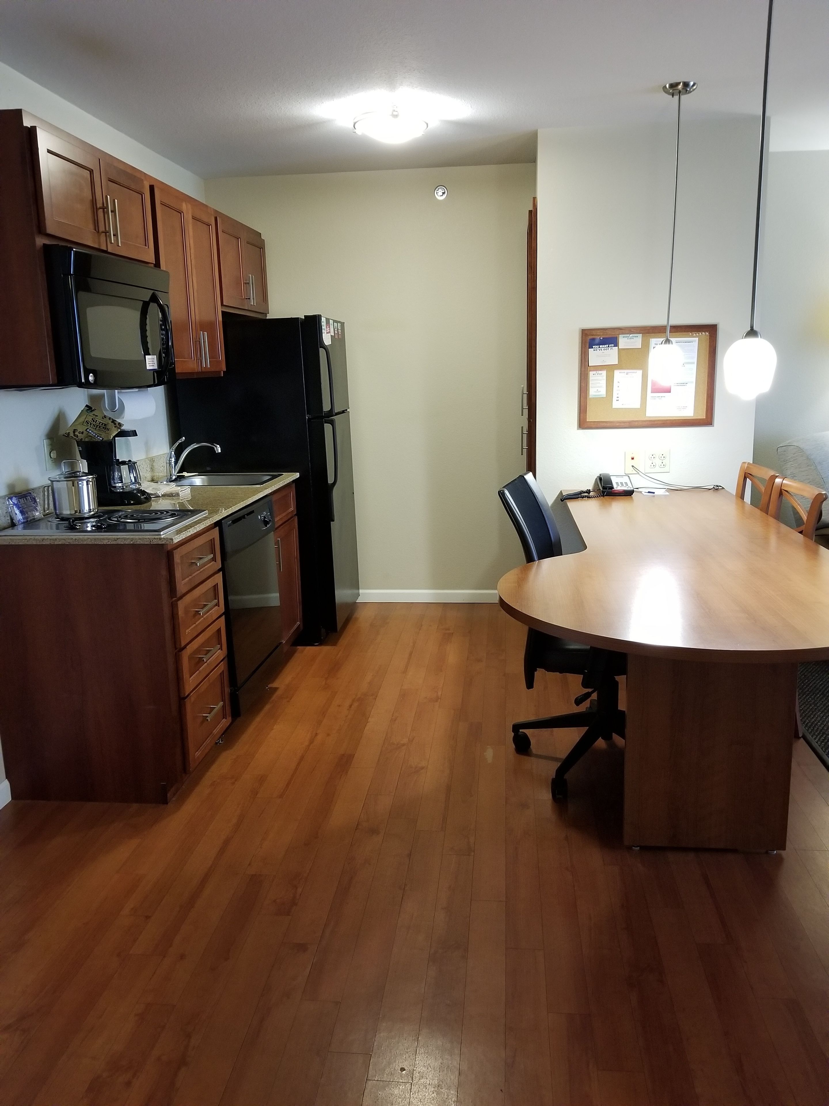 A kitchen with wooden cabinets, a black refrigerator, a stove, and a dining table with chairs.