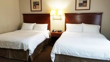 Una habitación de hotel con dos camas, cada una con ropa de cama blanca y cabeceros de madera. Hay dos mesitas de noche con lámparas y un teléfono.