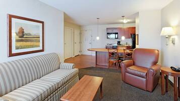 A hotel room with a sofa, armchair, dining table, and kitchen area.