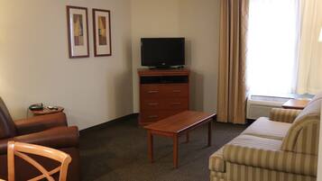 A hotel room with a sofa, a chair, a television on a wooden stand, and a small table.