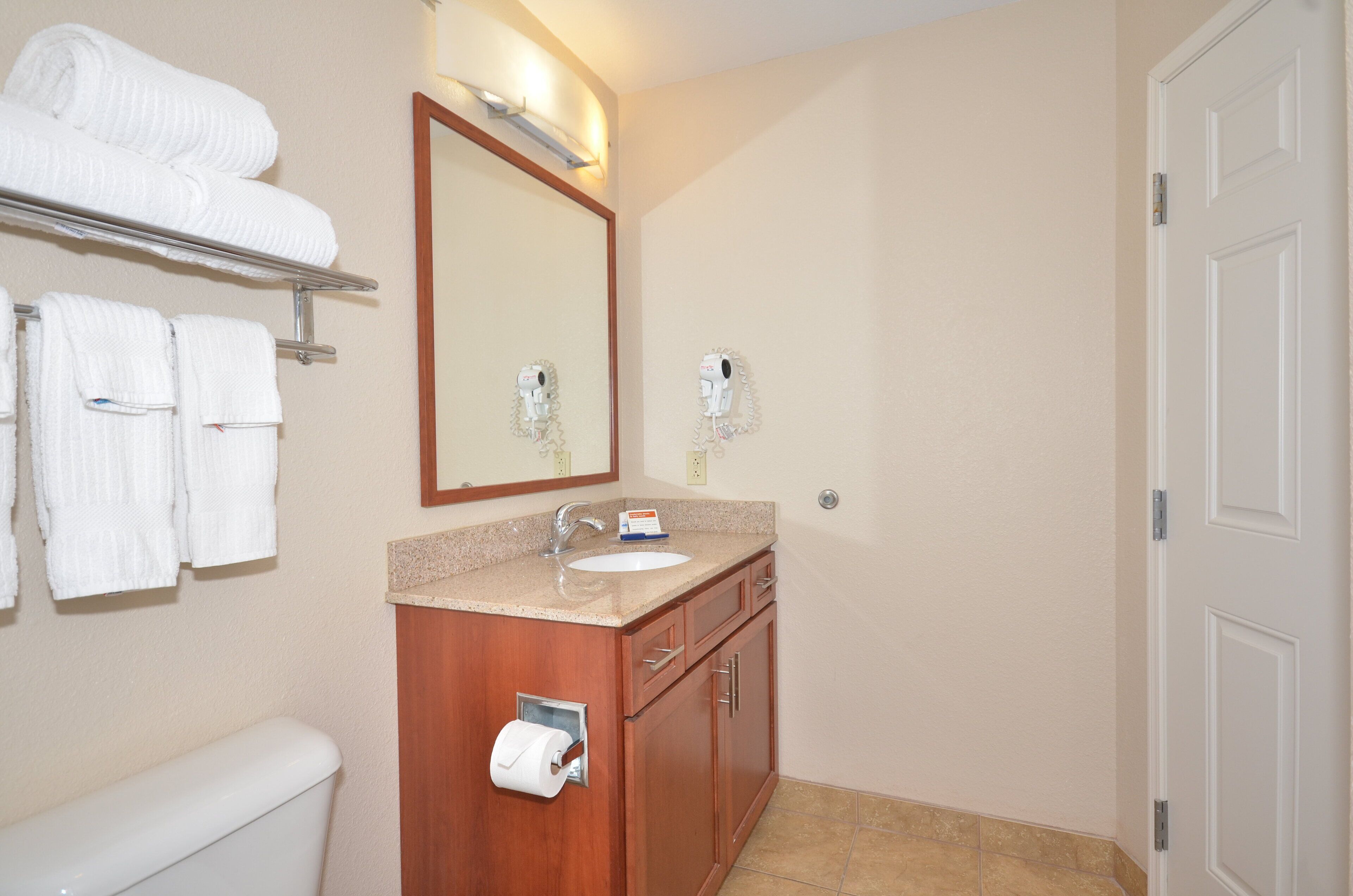 A bathroom with a toilet, sink, and mirror. There are towels hanging on a rack and a hairdryer mounted on the wall.