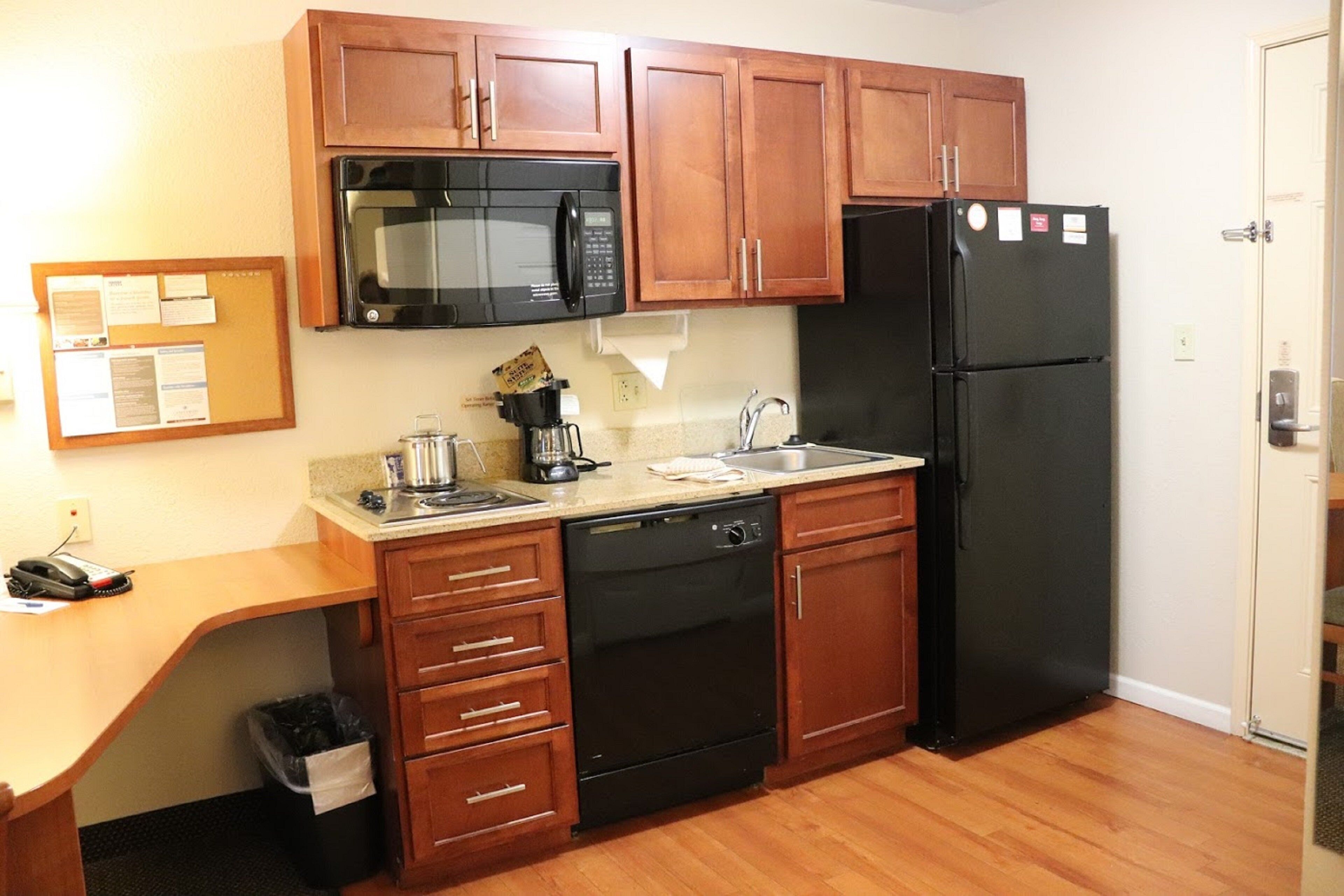 A compact kitchen with wooden cabinets, a black microwave, a refrigerator, and a coffee maker.