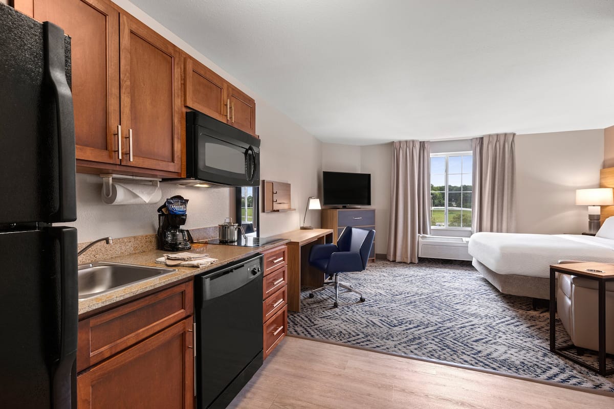 A hotel room with a kitchenette, a bed, a desk, and a TV.