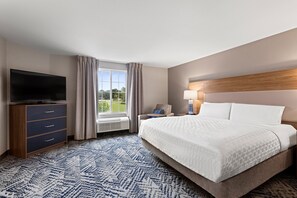 Habitación de hotel con cama, televisión, escritorio, lámpara y ventana con cortinas.