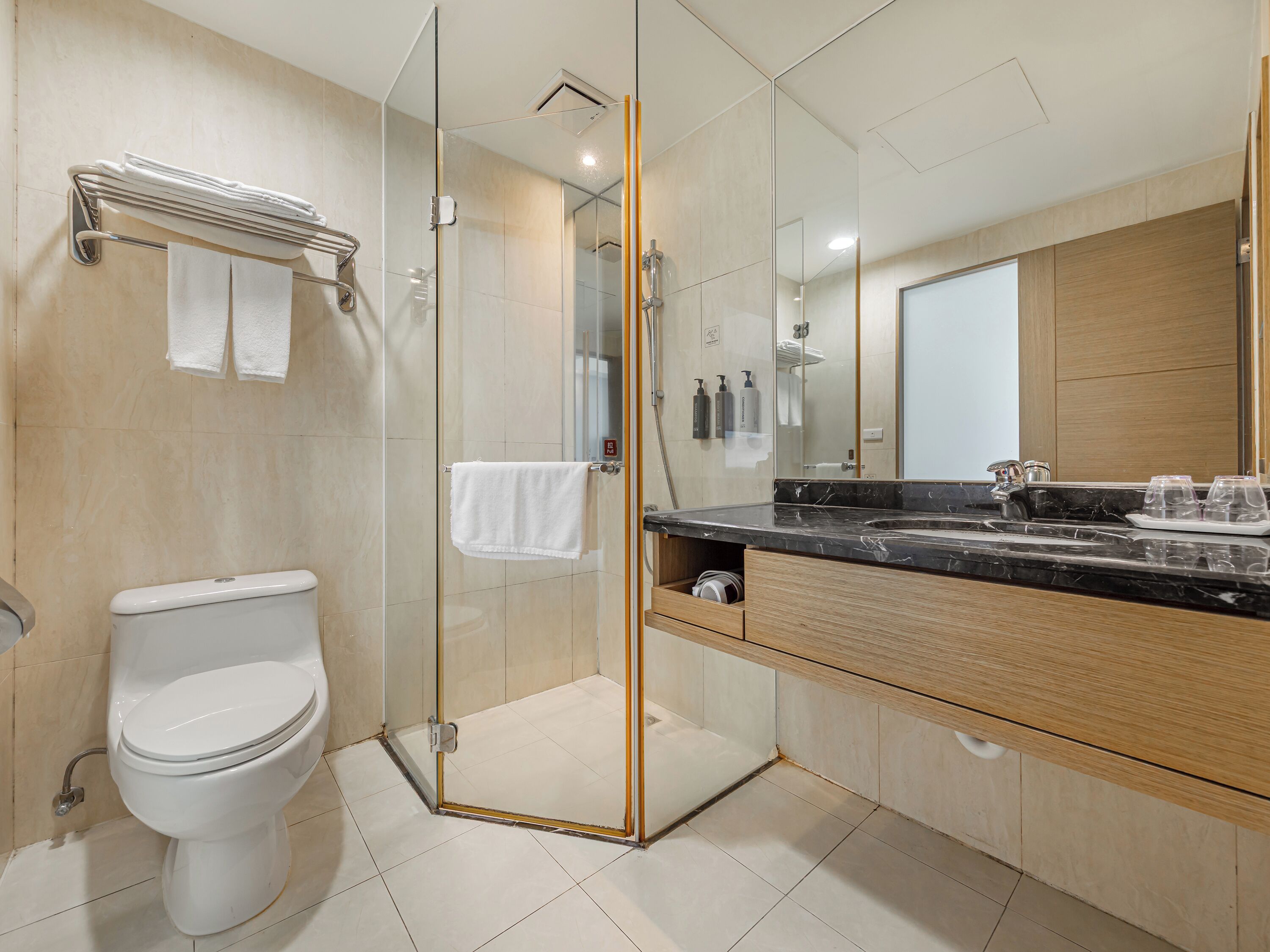 A modern bathroom with a glass-enclosed shower, a white toilet, a marble sink, and a wooden vanity.