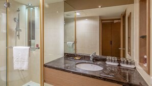 Une salle de bain moderne avec une douche en verre, un grand miroir et un lavabo en marbre agrémenté d’articles de toilette.