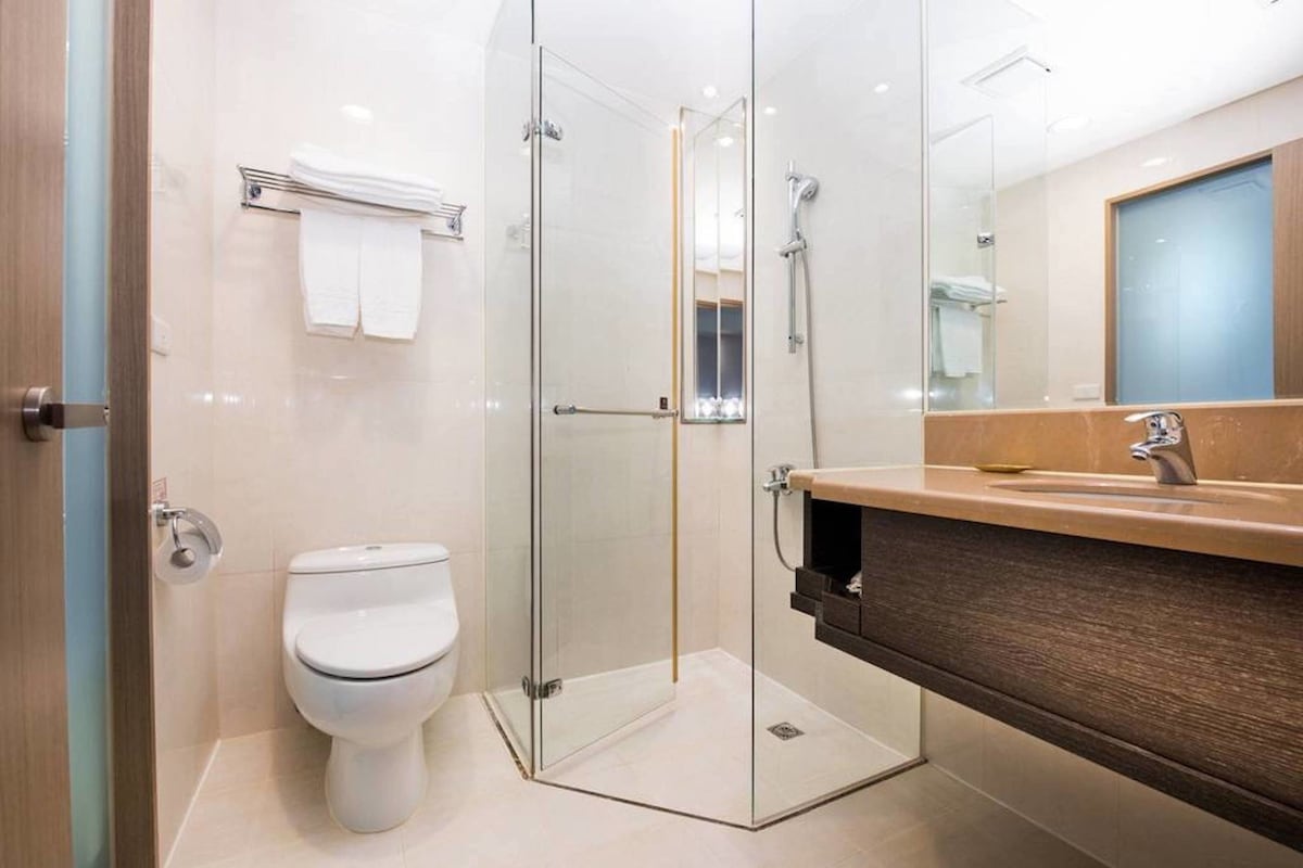 Un baño moderno con cabina de ducha de vidrio, inodoro blanco y tocador de madera con espejo.