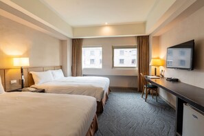 A hotel room with two beds, a desk, a chair, a television, and two windows with curtains.