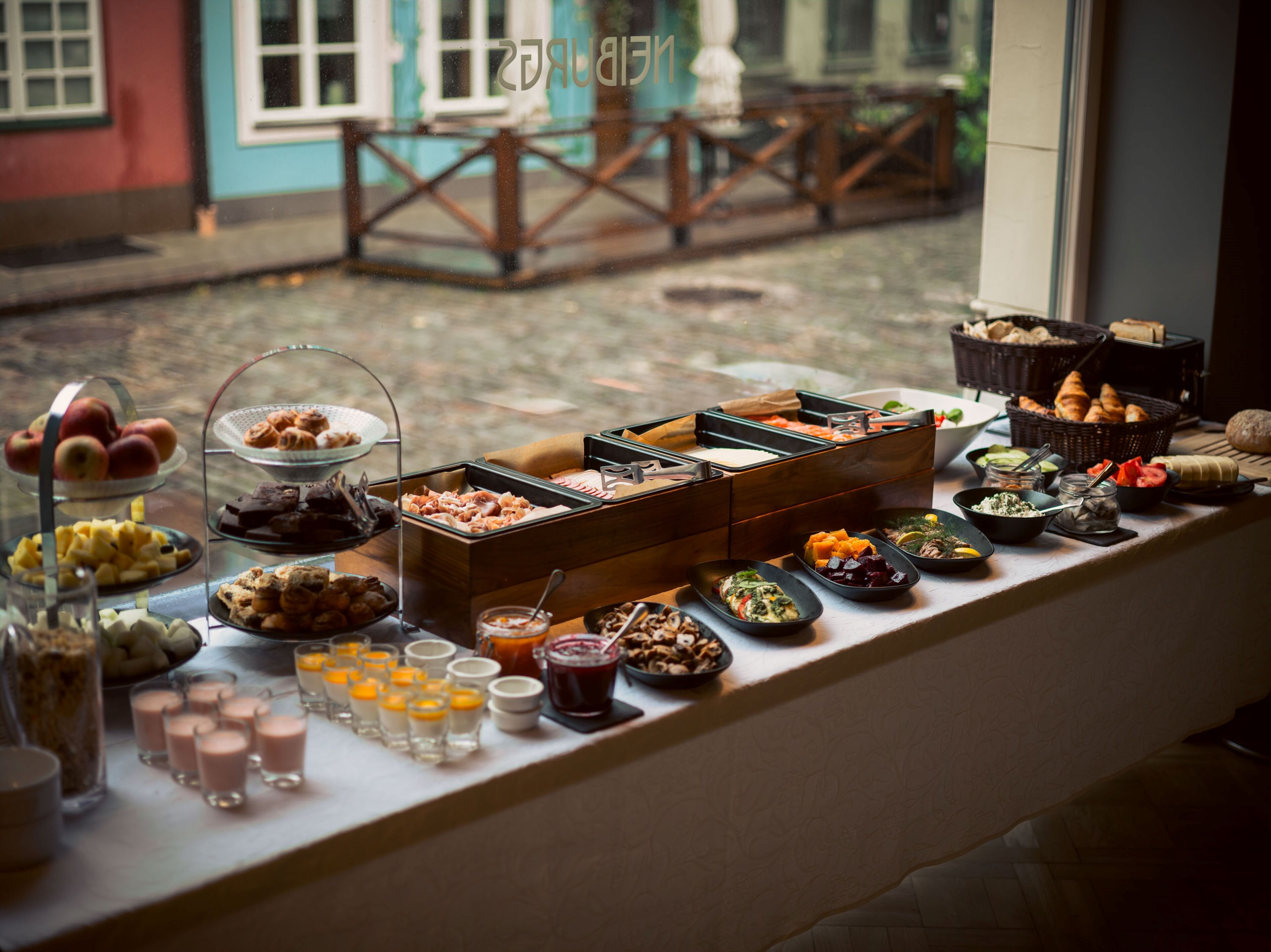 A buffet with various food items and drinks arranged on a table by a window.