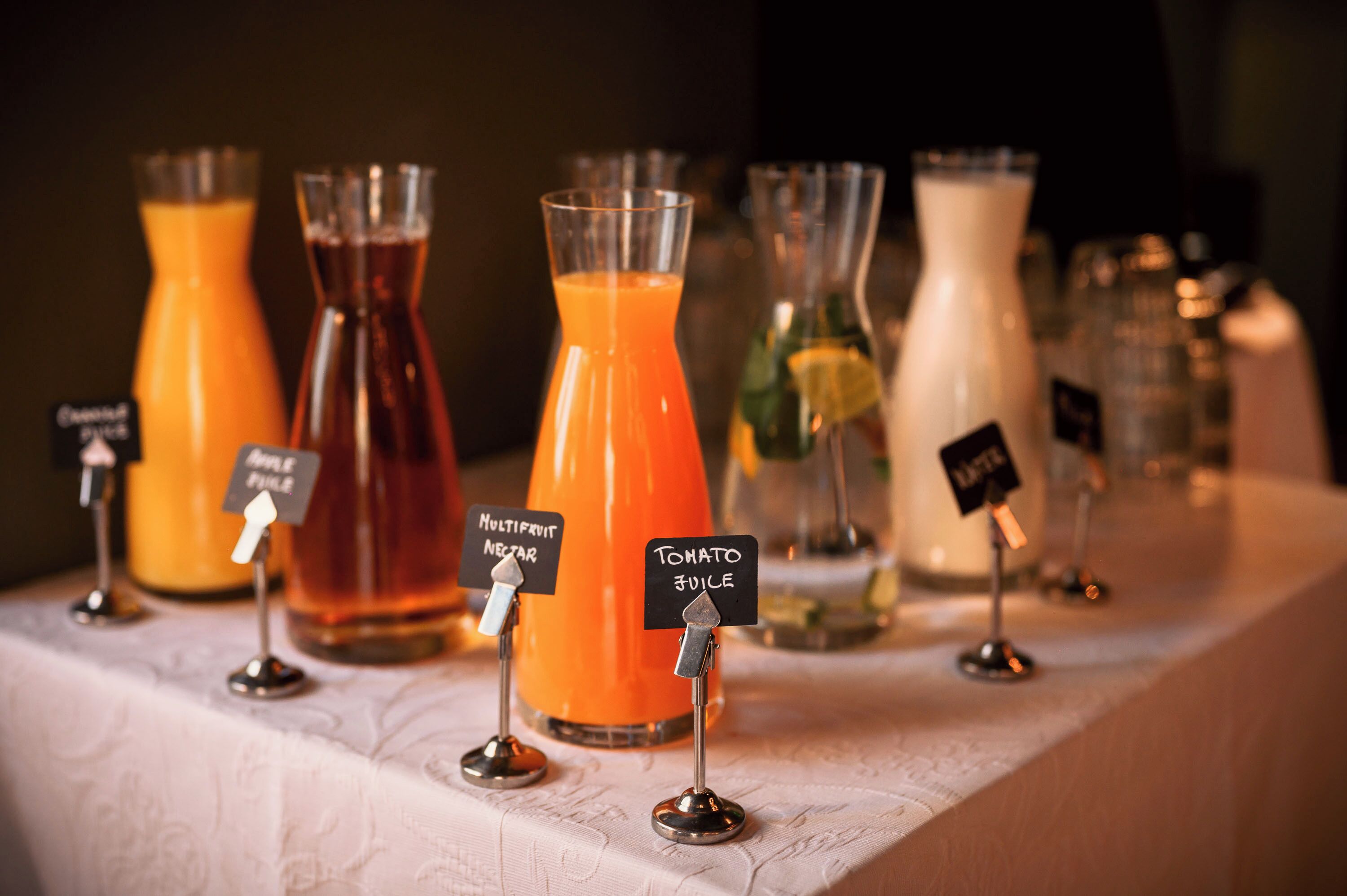 A beverage station with labeled dispensers for apple juice, multivitamin nectar, and tomato juice.