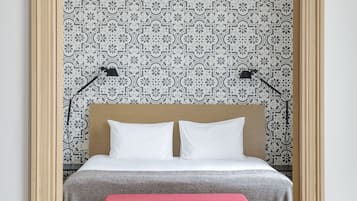 Un dormitorio con una cama, un banco rojo, una lámpara colgante y papel tapiz estampado.