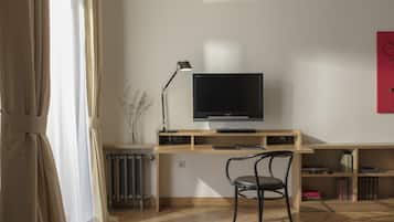 Una sala de estar moderna con un escritorio de madera, una silla negra, un televisor de pantalla plana, un radiador y una estantería.