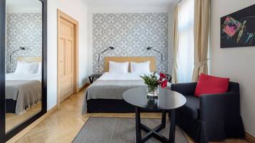 A hotel room with a bed, a sofa, a table, and a mirror.