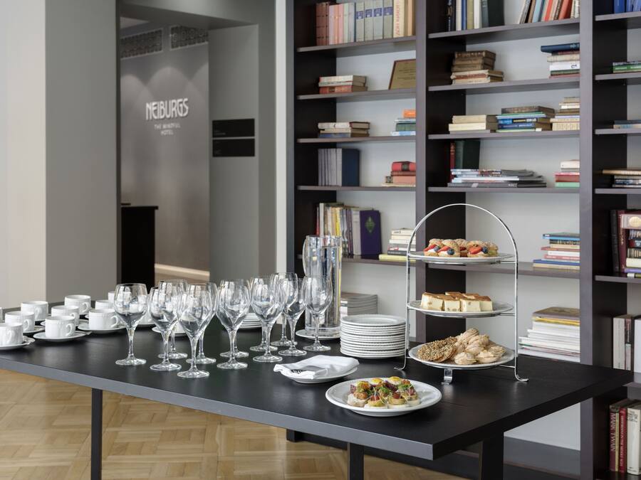 A table set with white cups, wine glasses, and plates of food, with a bookshelf in the background.