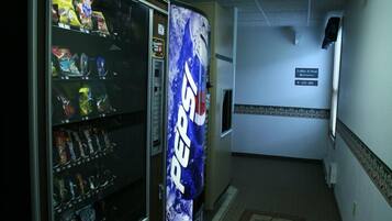 A hallway with a vending machine stocked with snacks and a Pepsi advertisement. A sign indicates the direction to the lobby and pool.