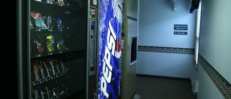 Un corridoio con una macchina distributrice piena di snack e una pubblicità di Pepsi. Un cartello indica la direzione verso la hall e la piscina.