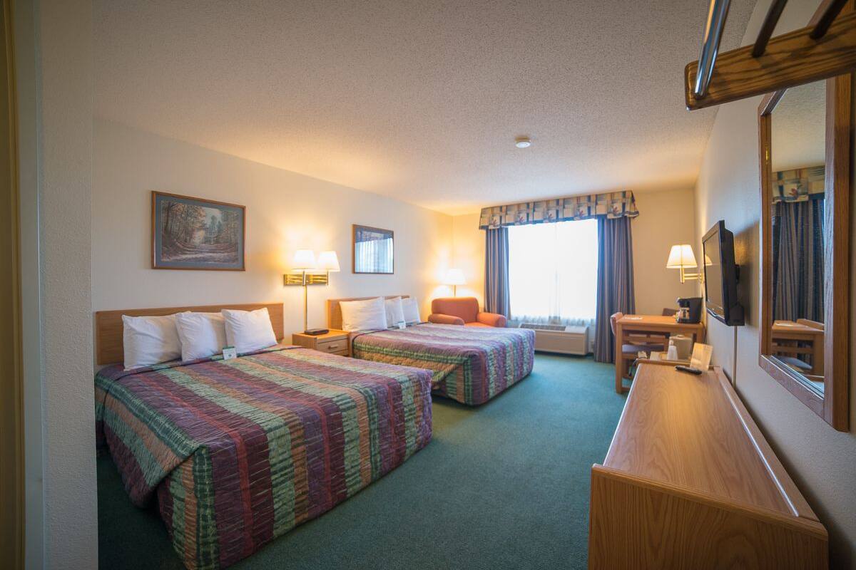 A hotel room with two beds, a desk, a chair, and a television.