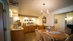 A kitchen with wooden cabinets, a dining table with chairs, a chandelier, and a wall sign that says "ENJOY". - River Valley Inn & Suites (Osceola)