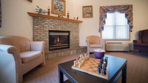 A living room with a fireplace, a chessboard, and two armchairs. - River Valley Inn & Suites (Osceola)