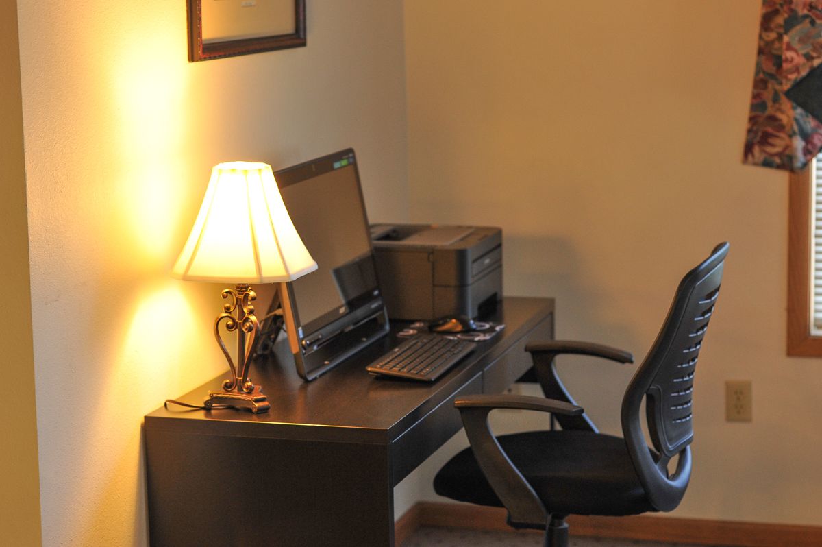 Un bureau avec un ordinateur portable, une imprimante et une lampe dans une chambre d’hôtel.