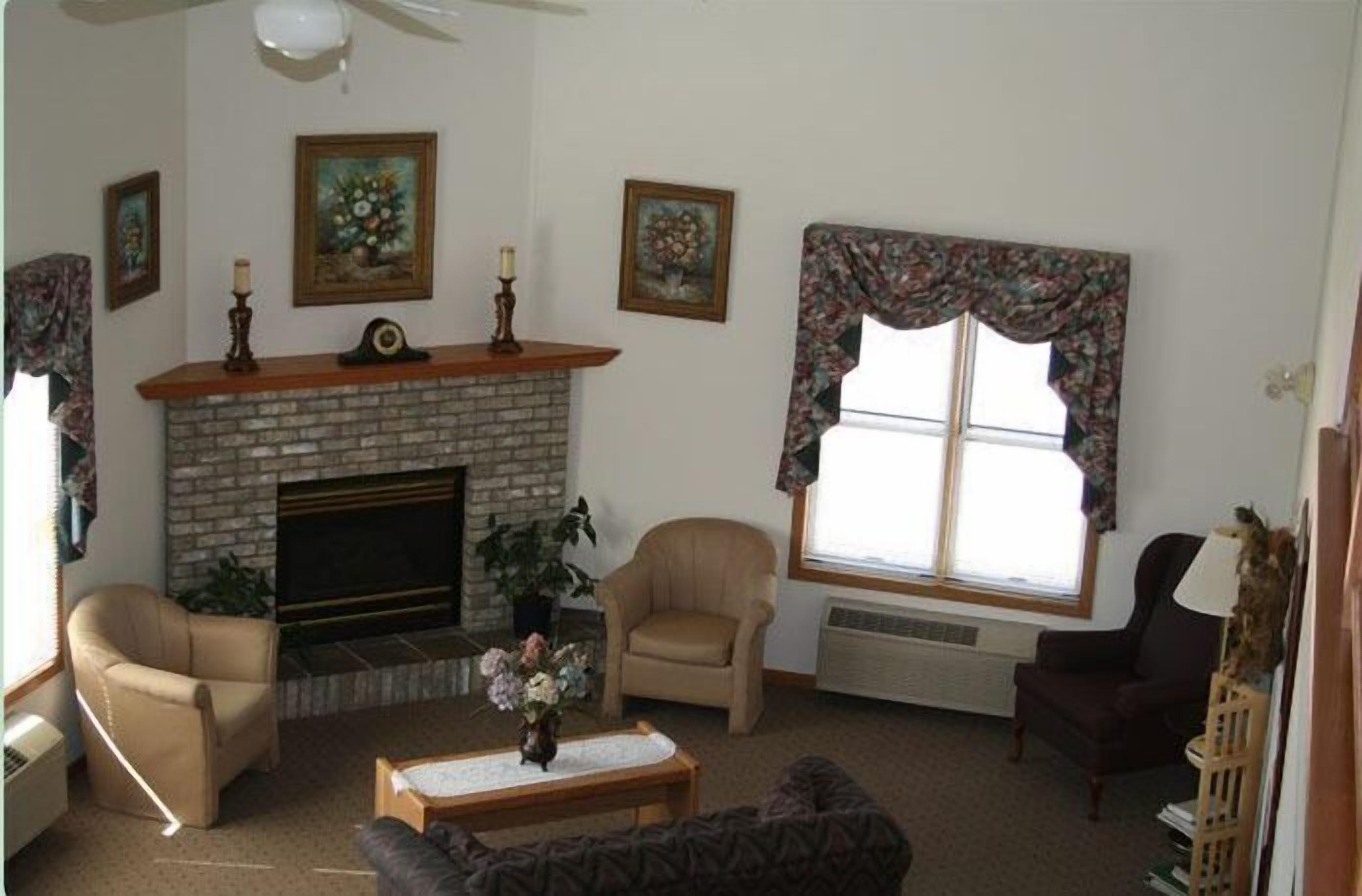 A living room with a fireplace, two armchairs, a sofa, a coffee table, and a large window with floral curtains.