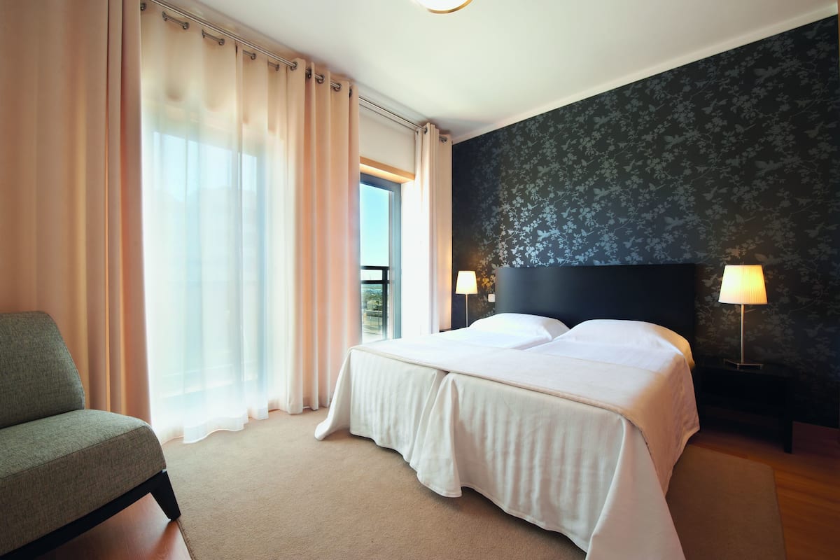 A hotel room with a bed, a chair, and a view of the outdoors.