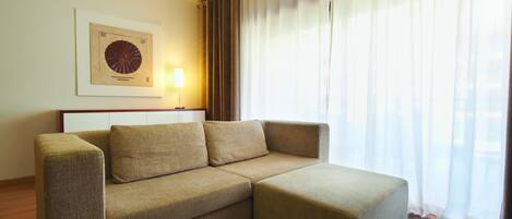 A modern living room with a sectional sofa, a framed artwork on the wall, and a large window with sheer curtains.