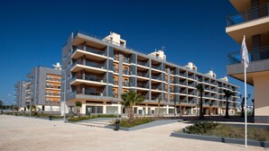 A multi-story hotel with balconies, a paved courtyard, and a flagpole. - Real Marina Residence (Olhao)