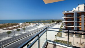 A modern building with a balcony overlooking a coastal road and the sea. - Real Marina Residence (Olhao)