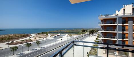 A modern building with a balcony overlooking a coastal road and the sea.