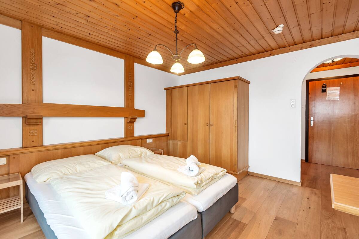 Een tweepersoonsbed met witte lakens en handdoeken, een houten garderobe en een houten plafond met een lamp.